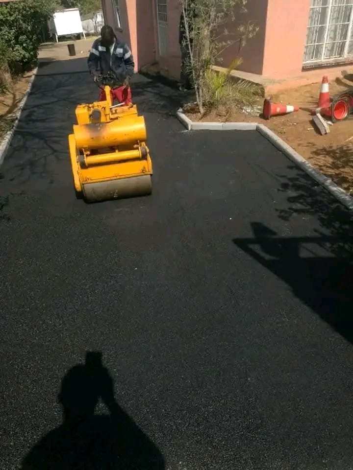 Small roller compacting a new tar driveway between concrete kerbs